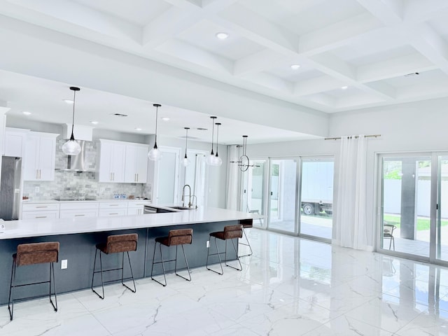 kitchen with wall chimney range hood, tasteful backsplash, black electric cooktop, a sink, and a breakfast bar