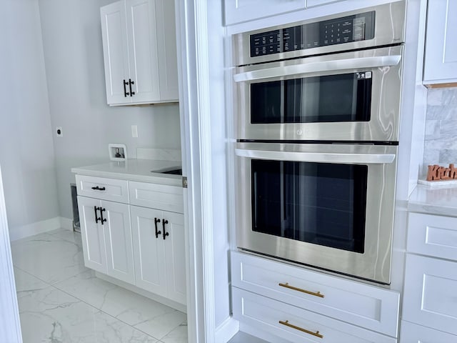 kitchen featuring light countertops, white cabinetry, stainless steel double oven, and marble finish floor