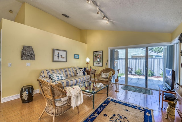 living room featuring hardwood / wood-style flooring, vaulted ceiling, rail lighting, and a textured ceiling