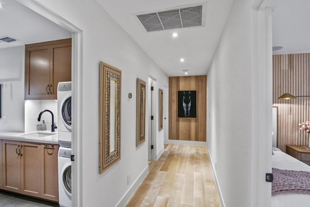 corridor with stacked washer / dryer, light wood-style flooring, visible vents, and a sink