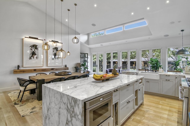 kitchen with light stone counters, a center island, stainless steel microwave, light wood-style floors, and a sink