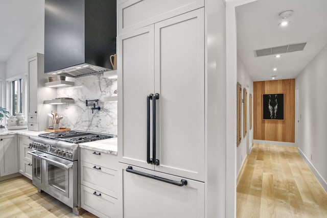 kitchen featuring wall chimney range hood, light wood-style flooring, visible vents, and range with two ovens