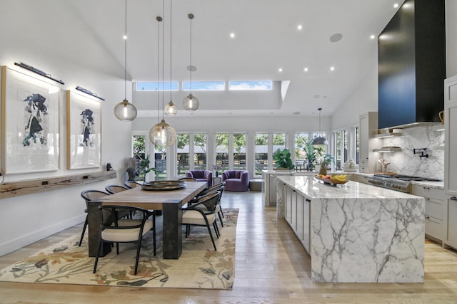 kitchen with light wood finished floors, light stone counters, range hood, high vaulted ceiling, and backsplash