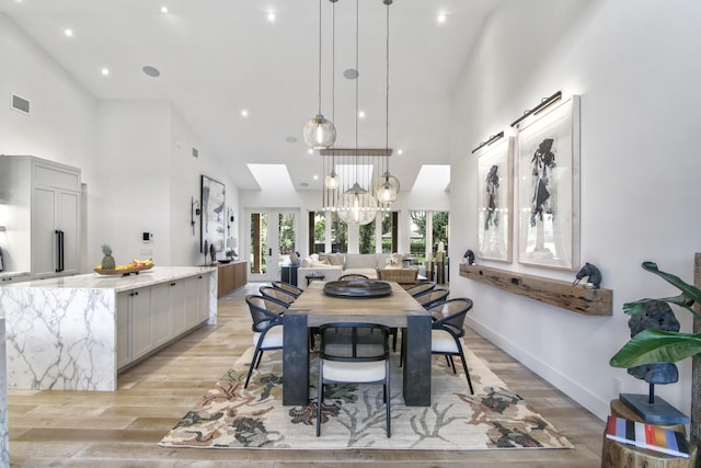 dining area featuring french doors, visible vents, a towering ceiling, and light wood finished floors