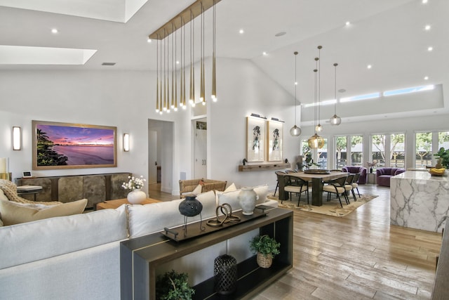 living area featuring a skylight, light wood-style flooring, visible vents, and high vaulted ceiling