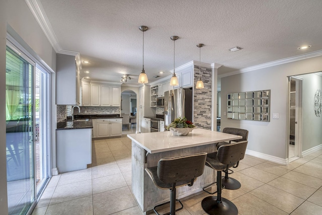 kitchen with appliances with stainless steel finishes, ornamental molding, light tile patterned flooring, and hanging light fixtures