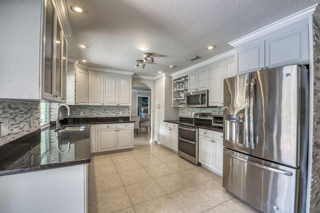 kitchen with appliances with stainless steel finishes, light tile patterned floors, sink, and white cabinets