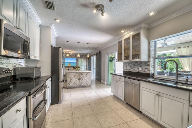 kitchen with sink, stainless steel appliances, a barn door, white cabinets, and hanging light fixtures