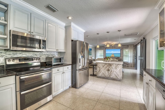 kitchen featuring appliances with stainless steel finishes, ornamental molding, decorative light fixtures, a barn door, and white cabinetry