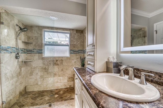 bathroom with a textured ceiling, crown molding, vanity, and a tile shower