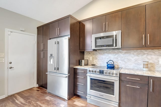 kitchen with dark brown cabinetry, stainless steel appliances, light stone countertops, and decorative backsplash