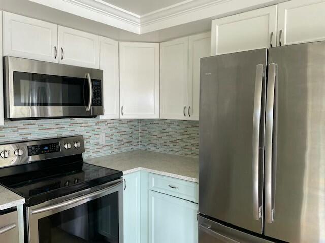 kitchen featuring light countertops, appliances with stainless steel finishes, decorative backsplash, and crown molding