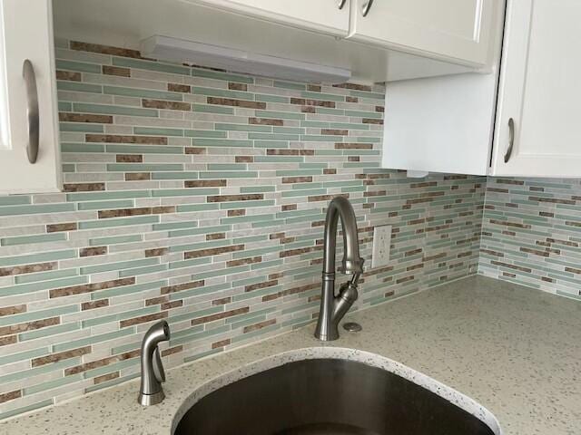 details featuring white cabinets, a sink, decorative backsplash, and light stone countertops