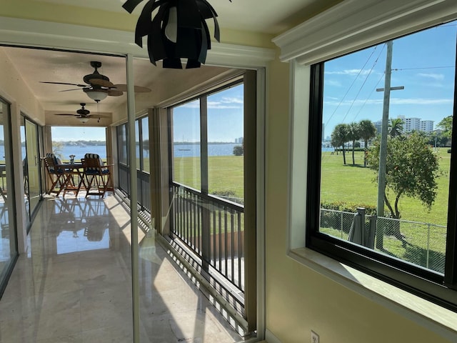 sunroom with ceiling fan and a water view