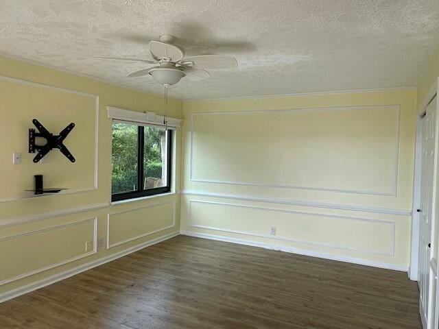 spare room featuring a textured ceiling, ceiling fan, wood finished floors, and a decorative wall