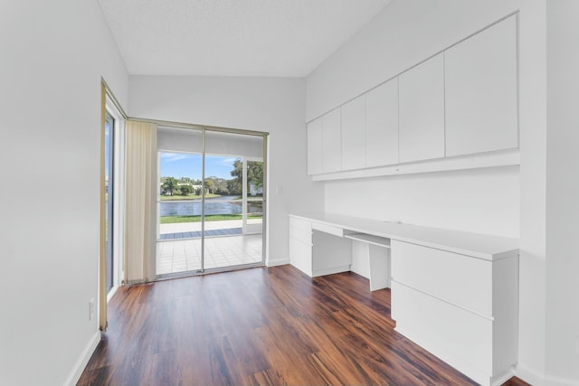 unfurnished office with a water view, dark hardwood / wood-style floors, built in desk, and a textured ceiling