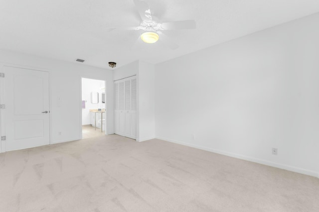 unfurnished bedroom featuring ensuite bathroom, light colored carpet, ceiling fan, and a closet