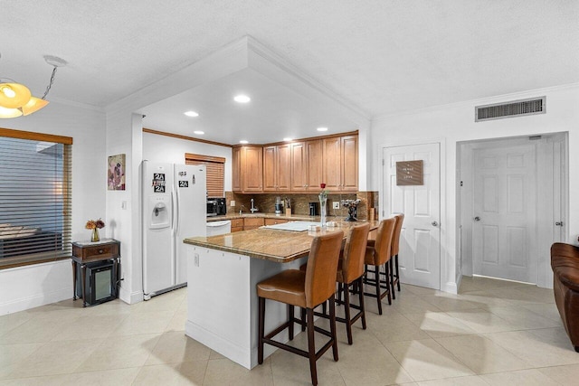 kitchen with visible vents, backsplash, a kitchen breakfast bar, a peninsula, and white appliances