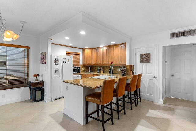 kitchen with visible vents, a kitchen breakfast bar, white refrigerator with ice dispenser, a peninsula, and decorative backsplash