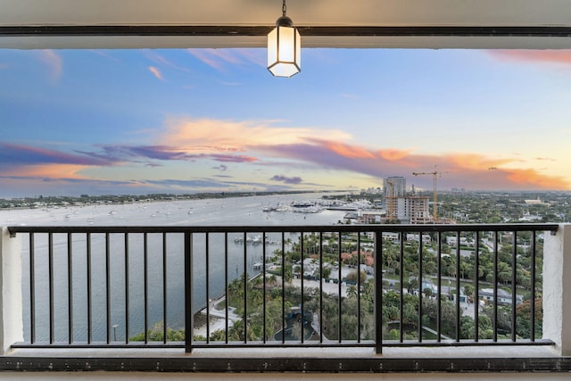 balcony at dusk featuring a water view