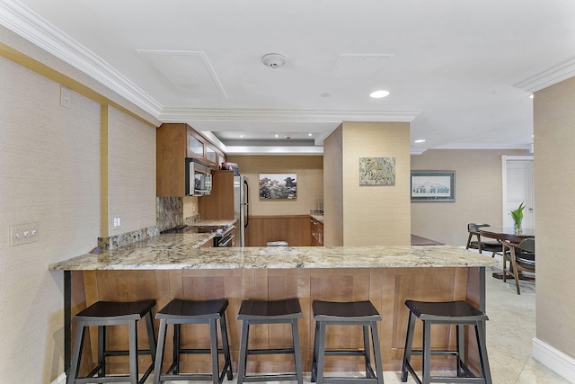 kitchen with stainless steel appliances, light stone counters, ornamental molding, a kitchen bar, and kitchen peninsula