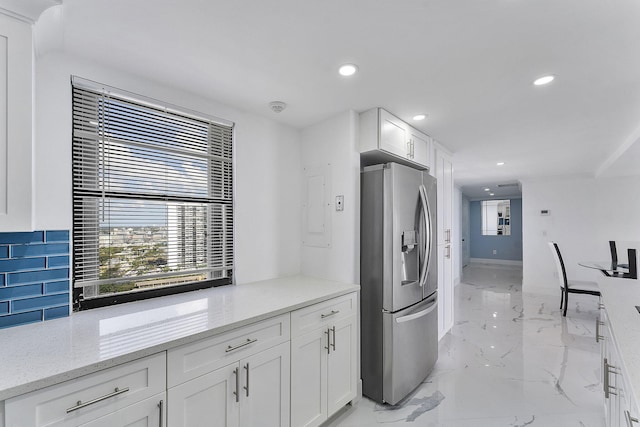 kitchen featuring tasteful backsplash, white cabinetry, stainless steel fridge, and light stone counters