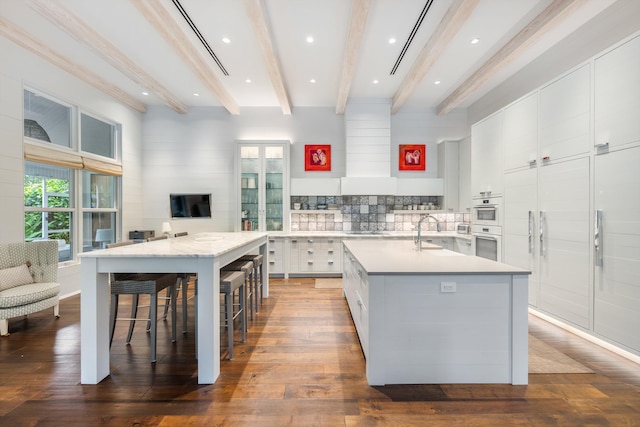 kitchen with sink, a breakfast bar area, hardwood / wood-style flooring, a kitchen island with sink, and white cabinets