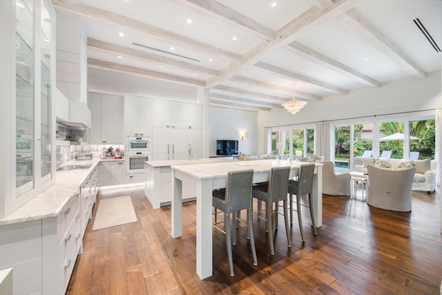 kitchen with dark wood-type flooring, a large island, light stone countertops, and white cabinets