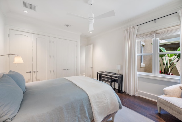 bedroom with dark hardwood / wood-style flooring, ceiling fan, ornamental molding, and multiple closets