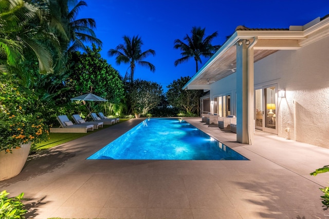 pool at night with a patio and outdoor lounge area