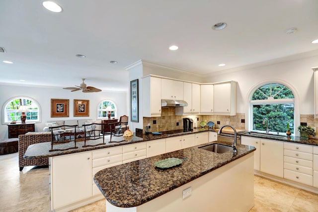 kitchen featuring dark stone countertops, an island with sink, sink, and white cabinets