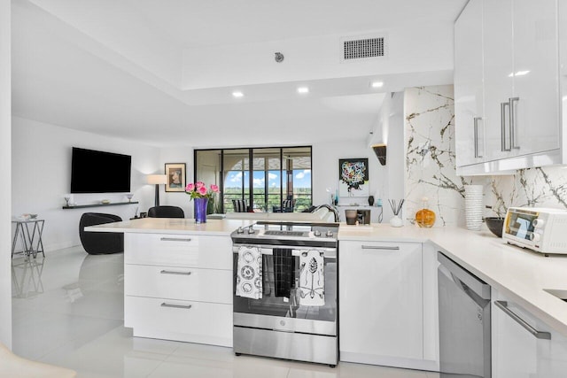 kitchen with appliances with stainless steel finishes, tasteful backsplash, a tray ceiling, white cabinets, and kitchen peninsula