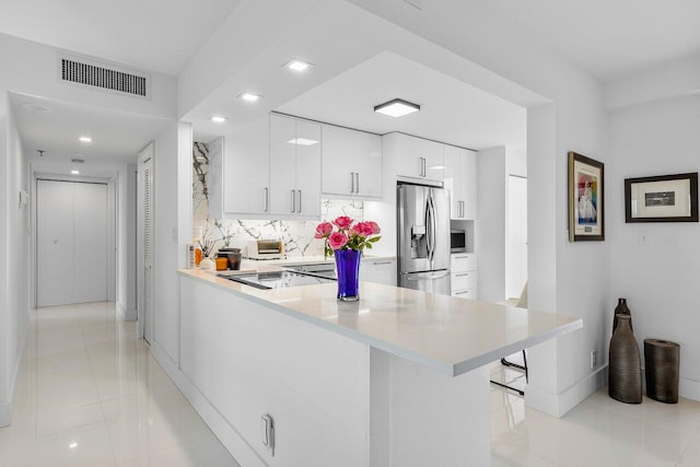 kitchen with stainless steel fridge, kitchen peninsula, white cabinets, and a kitchen bar