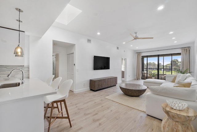 living room with ceiling fan, sink, light hardwood / wood-style floors, and a skylight