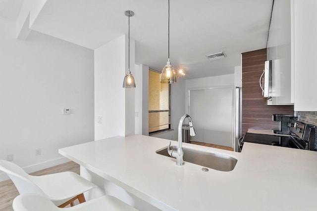 kitchen featuring pendant lighting, sink, a kitchen breakfast bar, kitchen peninsula, and electric stove