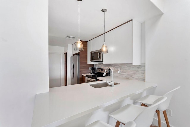 kitchen featuring sink, appliances with stainless steel finishes, a kitchen breakfast bar, white cabinets, and backsplash