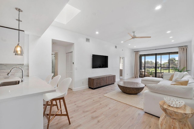 living room featuring ceiling fan, sink, light hardwood / wood-style floors, and a skylight