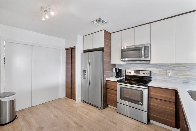 kitchen with white cabinetry, light wood-type flooring, tasteful backsplash, and appliances with stainless steel finishes