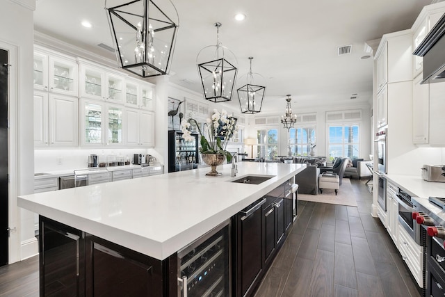 kitchen featuring pendant lighting, sink, wine cooler, an island with sink, and white cabinets