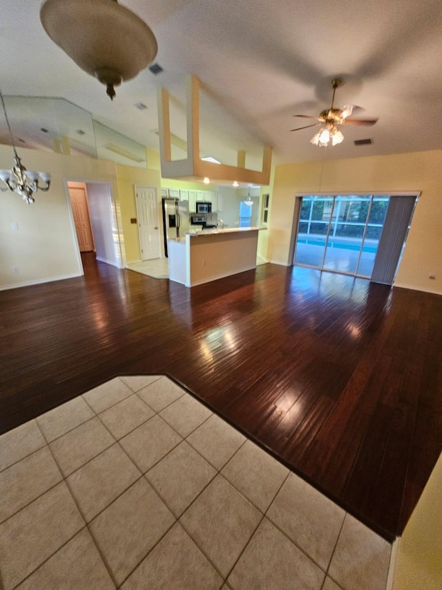 unfurnished living room with vaulted ceiling, wood-type flooring, and ceiling fan with notable chandelier