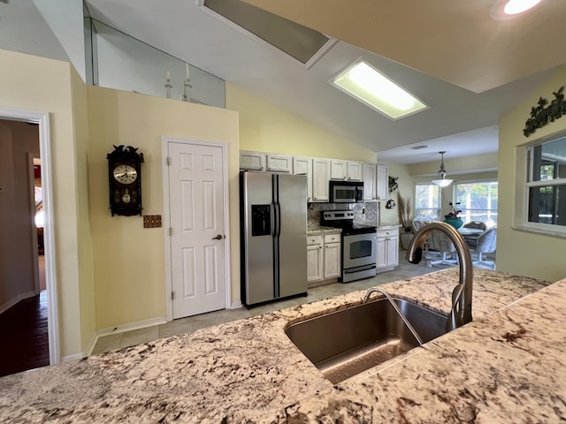 kitchen with sink, appliances with stainless steel finishes, white cabinetry, backsplash, and vaulted ceiling