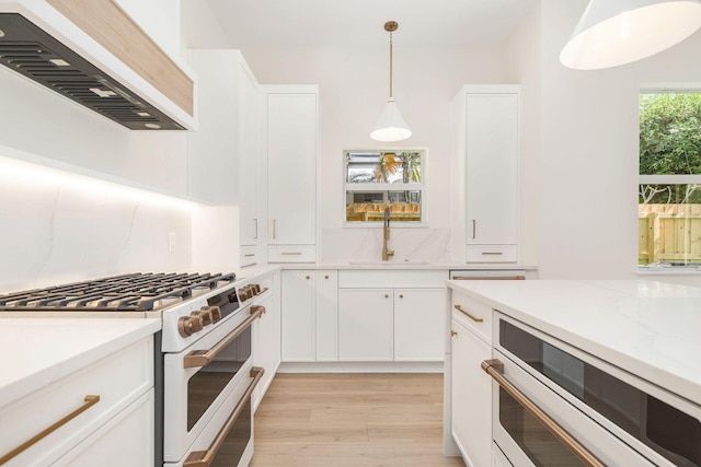 kitchen with light wood-type flooring, white gas range, extractor fan, pendant lighting, and a sink