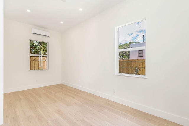 empty room with a wall mounted AC, light wood finished floors, and baseboards