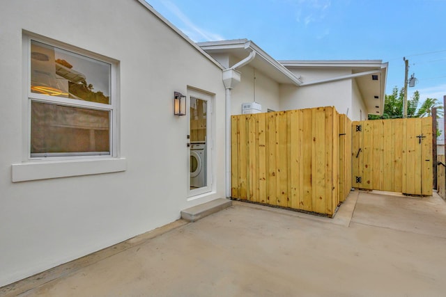 view of side of property with a patio, stucco siding, fence, and washer / dryer