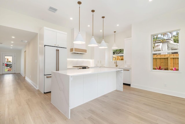 kitchen featuring a center island, light countertops, high end white fridge, white cabinetry, and light wood finished floors