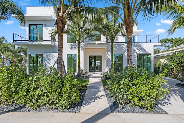 contemporary home with french doors, a balcony, and stucco siding