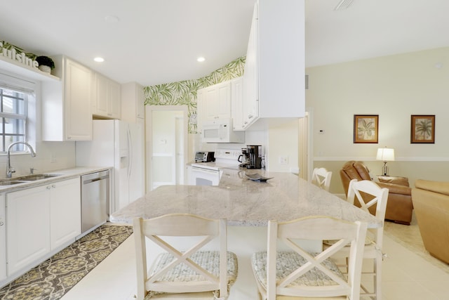 kitchen with sink, white appliances, a breakfast bar, and white cabinets