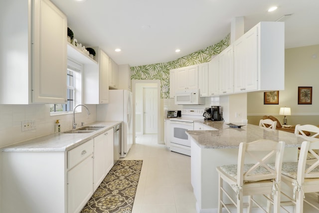 kitchen featuring sink, white appliances, a breakfast bar, white cabinets, and kitchen peninsula