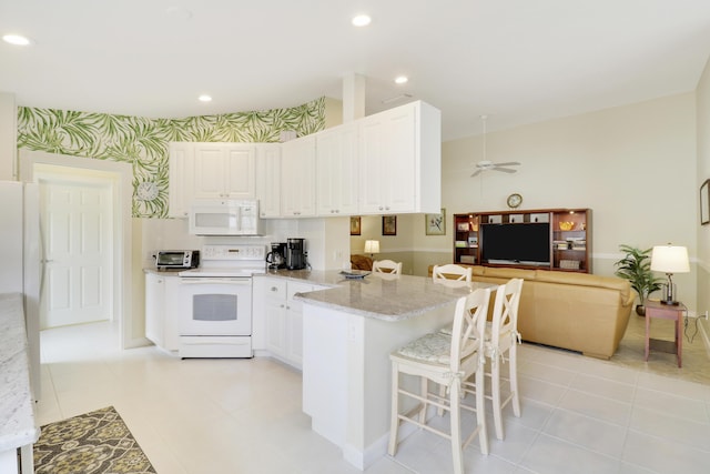 kitchen with white cabinetry, a kitchen breakfast bar, light stone counters, ceiling fan, and white appliances