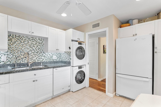 kitchen with white cabinetry, stacked washer and clothes dryer, sink, and white appliances